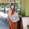 Anabaglish Bonnie Rattan Tote bagHand-crocheted rattan tote with blue embroidery, scalloped edges, cotton lining, and wide straps. Lightweight, roomy on young woman's shoulder. 