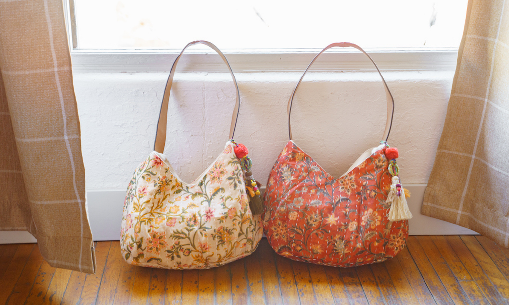 Two Anabaglish floral handbags hanging on a wall next to a window. Bags up to 70% off.
