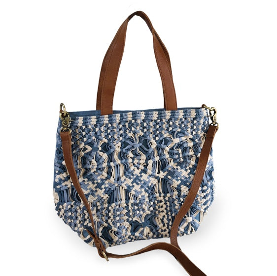 A denim blue and cream-colored macrame tote with leather straps and brass hardware, featuring a geometric diamond pattern.