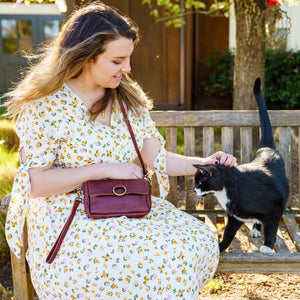 Woman sitting on a bench petting a cat wearing a brown crossbody bag, Sabrina Crossbody Bag.