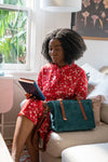 Woman in a red dress sitting on the couch reading a book with a teal suede bag next to her, Aurora Suede Tote.