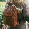 Small brown leather backpack on a woman at a flower garden, Addie Leather backpack.