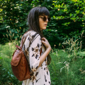 backpack on model outdoors with lush background, retro sunglasses, Addie Leather Backpack.