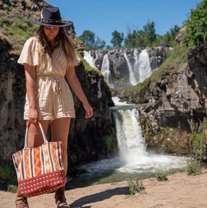 Woman in front of a waterfall holding a fabric tote, Cara Fabric Tote.