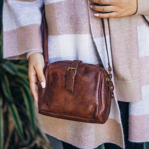 Close up image of a small  brown leather bag being worn by a woman, Sam Leather Crossbody Bag.