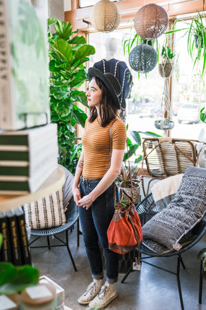 woman standing in a plant shop wearing a brick suede crossbody bag, Rowan Suede Crossbody Bag.